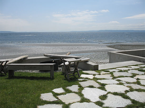 Driftwood benches surround a fire pit overlooking Puget Sound. Concrete stairs lead down to the beach.